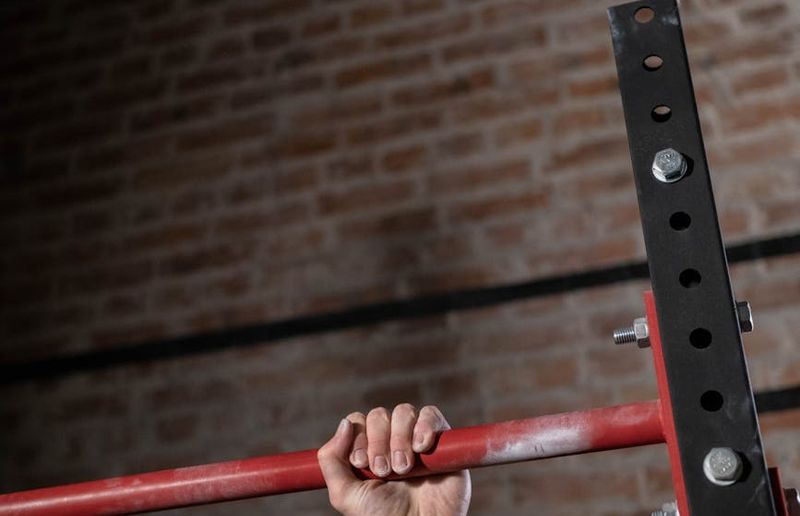 Close-up shot of a man's hands gripping a pull-up bar, showing muscle tension.